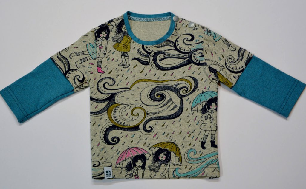Bunt bedrucktes Kinderoberteil mit Mädchen in Regenkleidung und blauem Rollkragen.